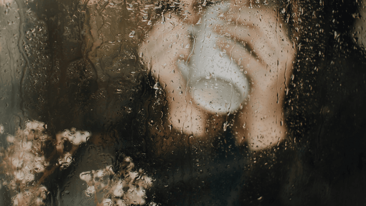 Mujer a través de una ventana mojada por la lluvia