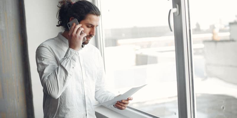 Hombre joven con camisa blanca, en una llamada telefónica sosteniendo un documento